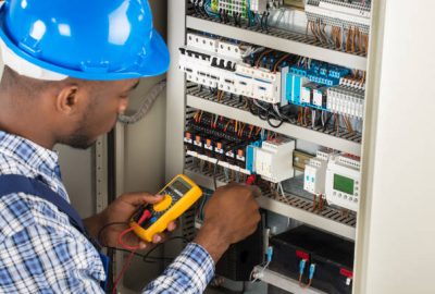 Close-up Of Male Electrician Checking Fuse Box With Multimeter